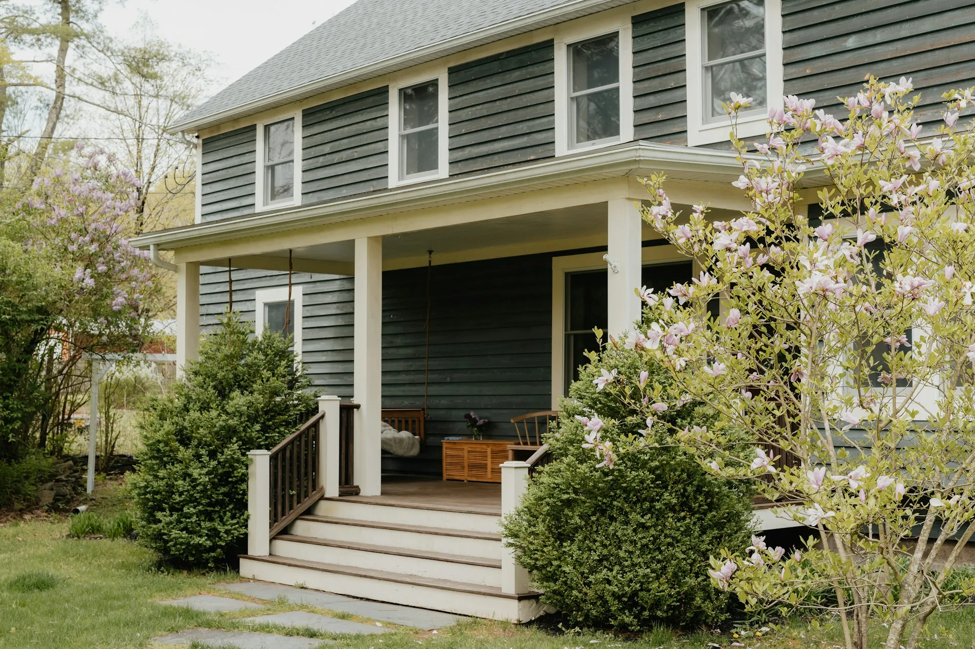 Gray two-story house with a covered porch and flowering shrubs