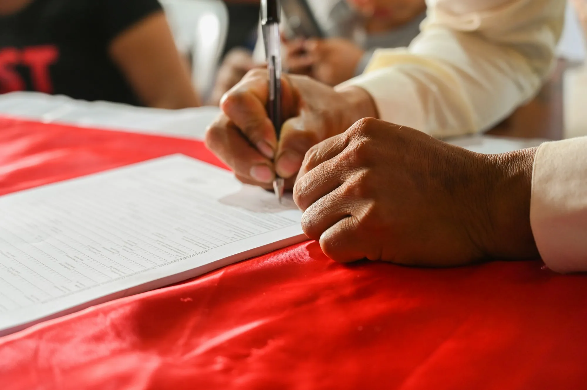 Hand signing papers on a red tablecloth